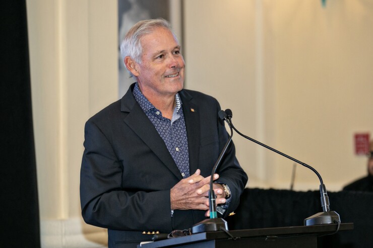 Javier D. Ferrer, the president and chief operating officer of Popular Inc., smiling with his hands crossed in front of a podium microphone.